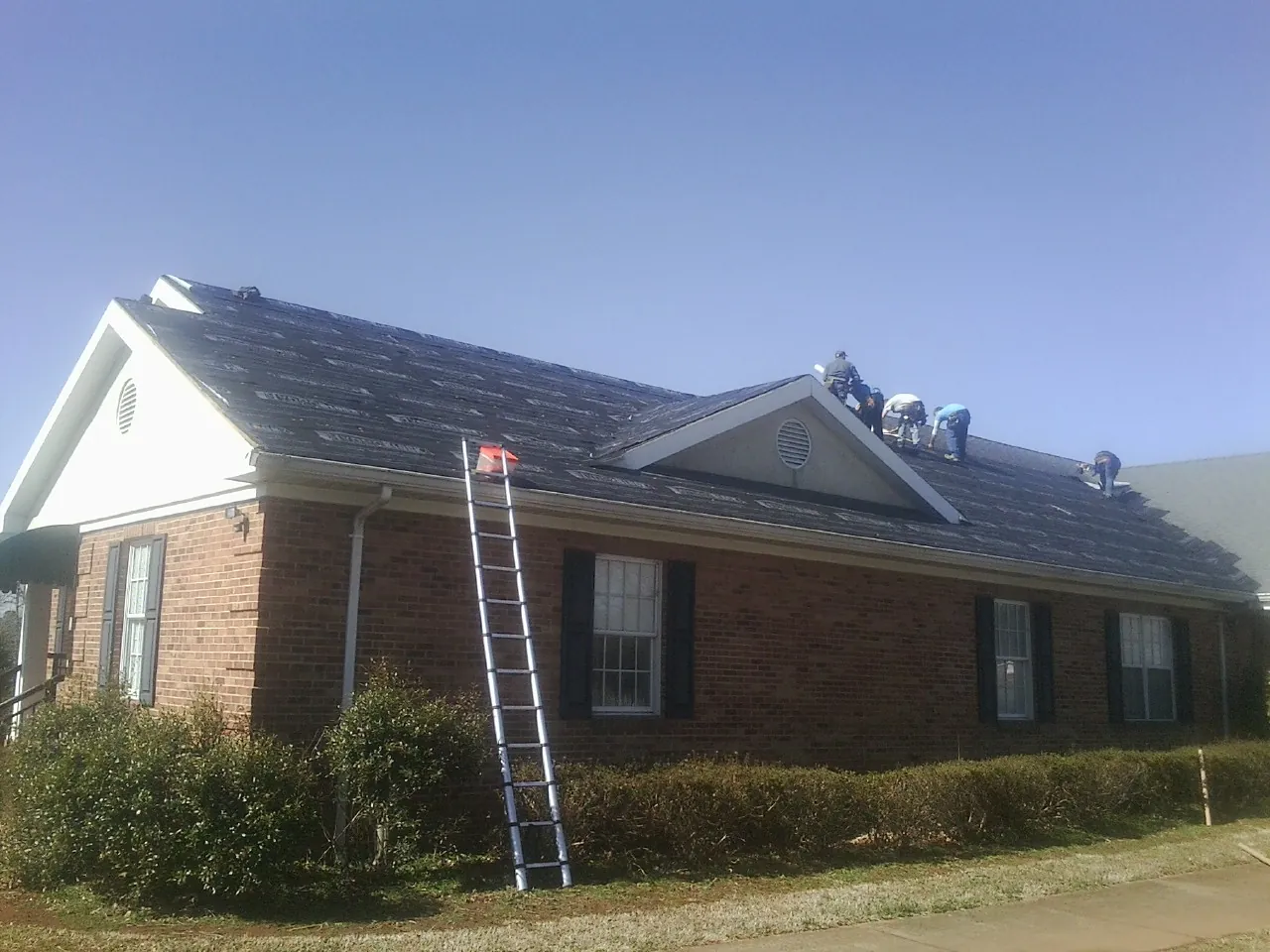 Crew tearing shingles off a brick ranch roof with a ladder set — Emergency Roof Repair work by our crew in Wells River