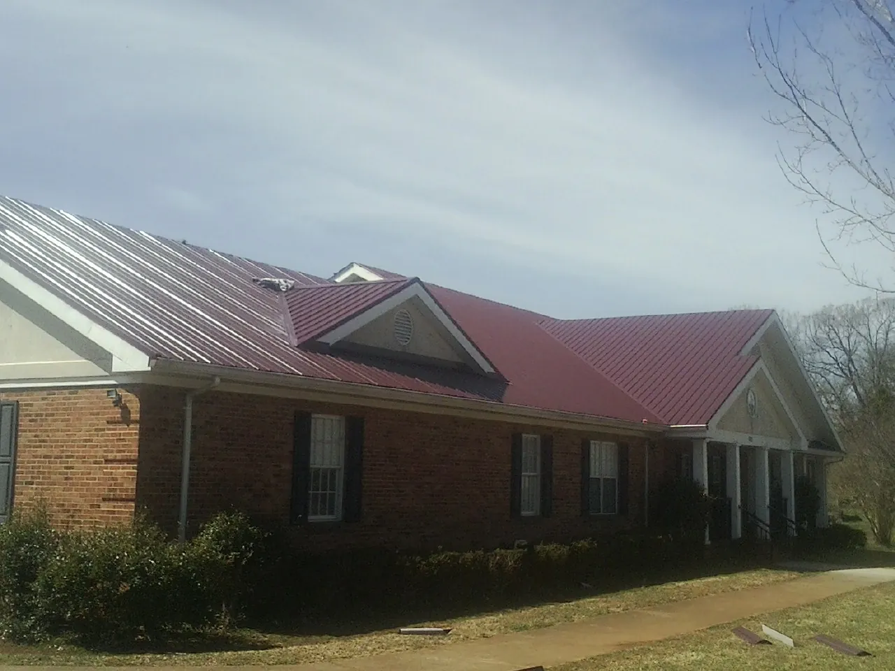 Red metal roof with gabled entries on a long brick building, from a Hail Damage Roof Repair job in Wells River