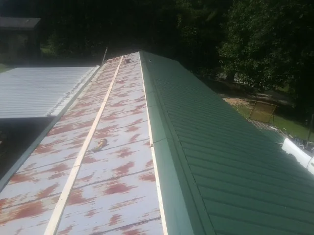 Old rusted panels beside newly installed green metal roofing — Wind Damage Roof Repair by Roofing Brothers in Wells River