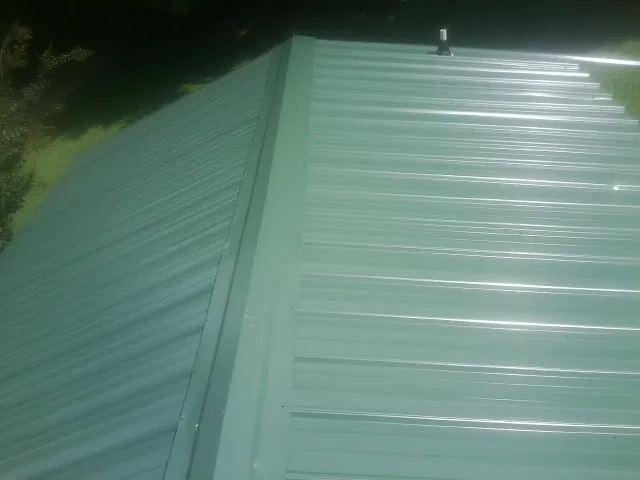 New green metal panels meeting at the ridge of a roof — Flat Roof Repair work by our crew in Wells River