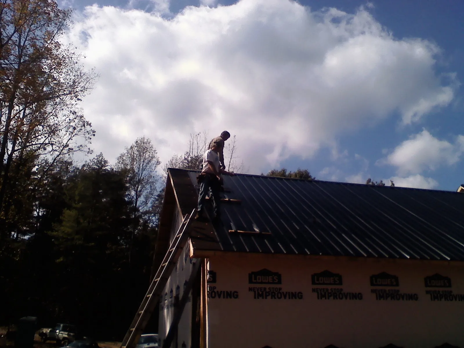 Roofer fastening dark metal panels high against a cloudy sky, from a Roof Inspection job in Wells River