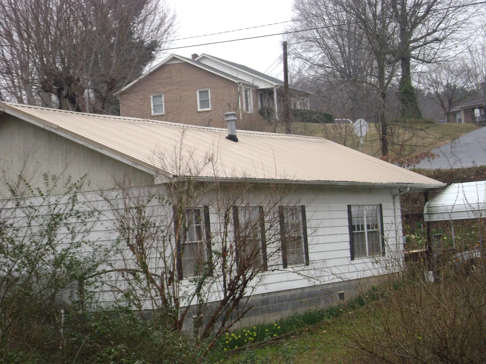 Tan metal roof on a white sided house set into a hillside — Commercial Roofing by Roofing Brothers in Wells River